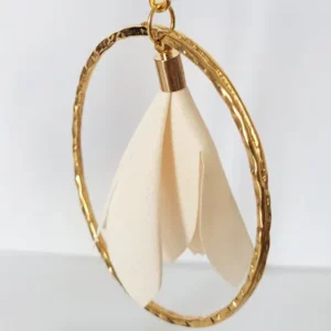 Boucles d'oreilles pendantes avec des supports en formes de 3 coeurs colorés en blanc et dorés. Ces supports ont un anneau martelé et un pompon en imitation satin de couleur beige à l'intérieur.