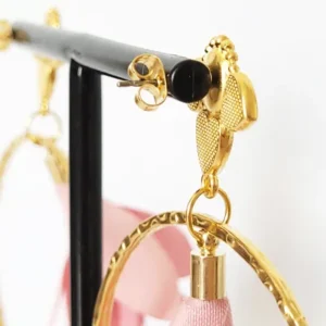 Boucles d'oreilles pendantes avec des supports en formes de 3 coeurs colorés en prune nacrée et dorés. Ces supports ont un anneau martelé et un pompon en imitation satin de couleur rose à l'intérieur.