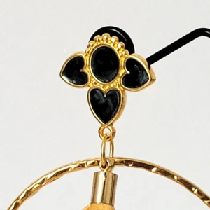 Vue sur le support des boucles d'oreilles pendantes avec des supports en formes de 3 coeurs colorés en blanc et dorés. Ces supports ont un grand anneau martelé et un pompon en imitation satin de couleur moutarde à l'intérieur.