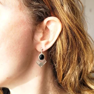 Vue portée des boucles d'oreilles argentées pendantes avec cabochon ovale noir en verre et triangle argenté ajouré